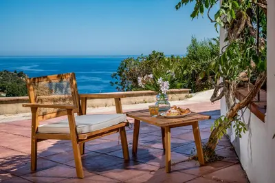 a wooden chair and a table on a patio with the ocean at Casa vinz in Scopello