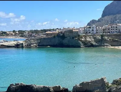 a beach with blue water and buildings in the background at Sicilia biedda casa vacanze in Terrasini