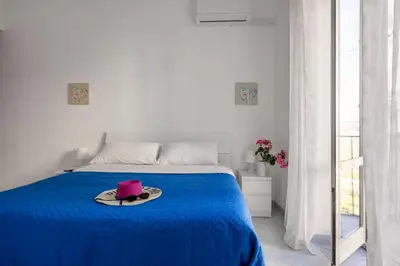 a white bedroom with a blue bed with a hat on it at La Castellana Apartments, vista panoramica sul mare, nel cuore storico di Carini, a due passi dal Duomo e dal castello in Carini