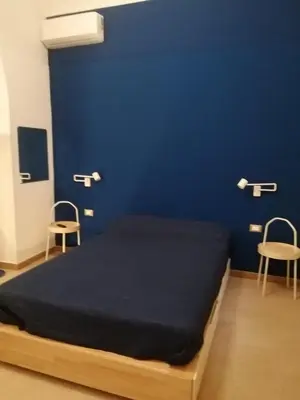 a bed in a room with two chairs and a blue wall at Domus Case Vacanze civico del mare in Castellammare del Golfo