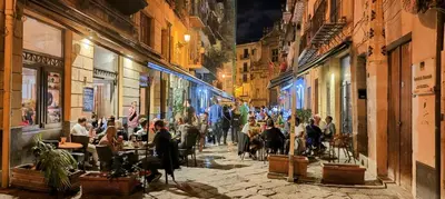a group of people sitting at tables on a street at night at Crihouse in Palermo