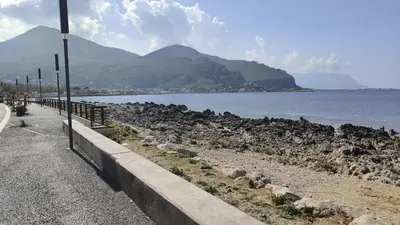 a road next to a body of water with mountains at Crihouse in Palermo
