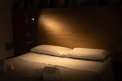 a bed with white sheets and pillows in a dark room at Appartamento completo con parcheggio privato - Villa Ciaculli in Villabate