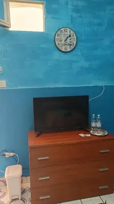 a clock on a blue wall above a dresser with a tv at LA TERRAZZA SUL MARE camera doppia vicino aereoporto&mare SICILIAN SEA STYLE ROOM in Cinisi