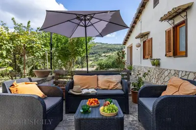 a patio with chairs and an umbrella and a table with fruit at La Gurra Tenuta Migliore By DomuSicily in Chiusa Sclafani
