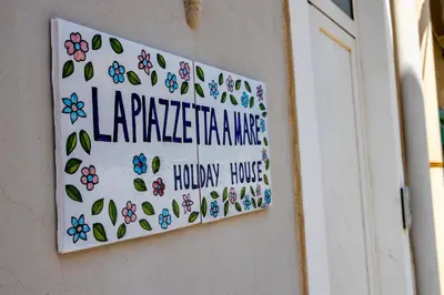 a sign on a wall with flowers and leaves at La Piazzetta a Mare Holiday House in Sferracavallo