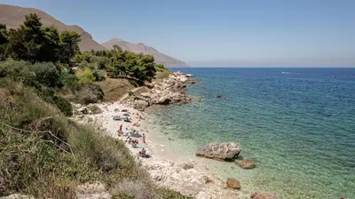 a group of people laying on a beach near the water at Villa Regina ai Faraglioni di Scopello in Scopello