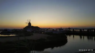 a sunset with a windmill next to a body of water at Casa Renda in Balestrate