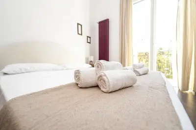 a white bedroom with two beds and a large window at Maison d'art Orleans in Palermo