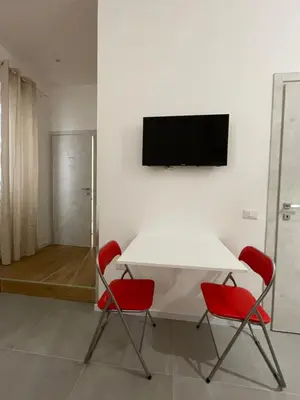 a white table with two red chairs and a television on a wall at My Happy Place Rooms in Palermo