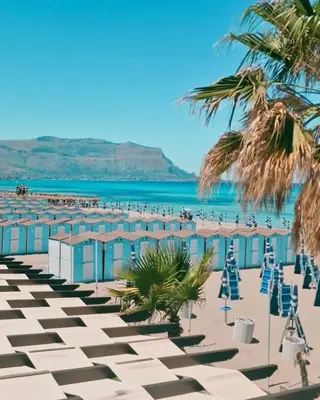 a beach with beach huts and palm trees and the ocean at Loriano Apartment in Capaci