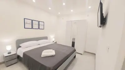 a white bedroom with a large bed and a television at Murriali Apartment in Monreale