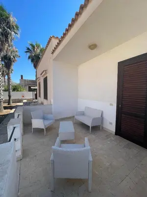 a patio with white furniture and palm trees at Appartamento Giglio in San Vito lo Capo