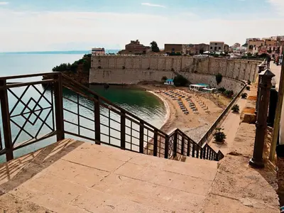 a beach with umbrellas and chairs next to a wall at Verdeacqua Home in Castellammare del Golfo