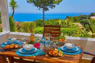 a wooden table with food and a view of the ocean at Villa Desirée - Scopello-Villas in Scopello
