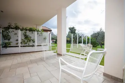 a porch with white chairs and a patio at Villa dell'Ulivo - by DomuSicily in Terrasini