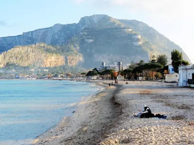a person sitting on a beach with a mountain in the background at Appartamento Blu in Palermo