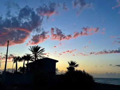 a sunset with palm trees and a building on the beach at traversa 8, aeroporto in Cinisi
