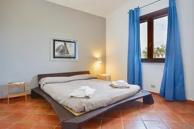a bedroom with a bed with blue curtains and a window at Villa del Drago in Scopello