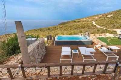 a wooden deck with a swimming pool and a table and chairs at Villa Scogliera Cala Bianca in Castellammare del Golfo