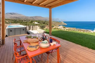 a red table on a deck with a view of the ocean at Villa Zingaro Cala Bianca in Castellammare del Golfo
