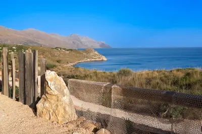 a fence and a rock on a hill next to the ocean at Villa Zingaro Cala Bianca in Castellammare del Golfo