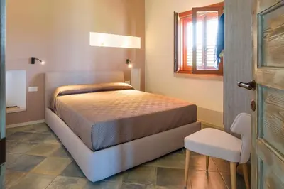 a bedroom with a bed and a chair and a window at Villa Scopello Cala Bianca in Castellammare del Golfo