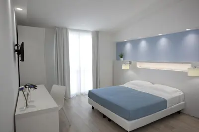 a white bedroom with a bed and a desk at Hotel Perla Gaia in San Vito lo Capo