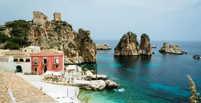 a red building in the water next to the ocean at Villa Berretta by Sicily Travelling Villas in Scopello