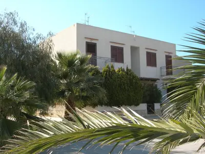 a white building with palm trees in front of it at Oasi del Sole- sun and sea - Casa Xenia in San Vito lo Capo