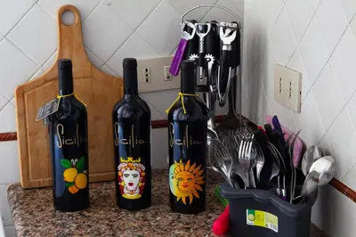 three bottles of wine on a counter with utensils at My House Holiday Apartment in Palermo