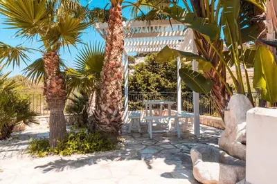 a white bench sitting between two palm trees at Villa con Piscina 150mt dal Mare 8 Posti OA in Alcamo
