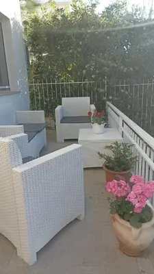 a patio with white wicker chairs and flowers in pots at MONDELLO JUNO'S ROOMS in Mondello