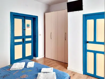 a room with a bed with blue doors and a tv at Don Vito's Apartments in Castellammare del Golfo