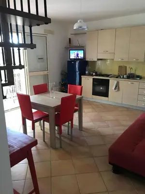 a kitchen and dining room with a table and red chairs at Villetta giardino, piscina, mare in Campofelice di Roccella