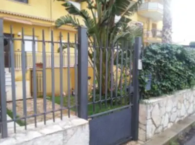 a fence with a palm tree in front of a building at Casa Ponticello in Termini Imerese