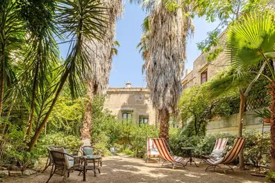 a garden with palm trees and chairs and a building at Principe di Castelnuovo Historical Suites in Palermo