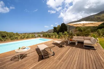 a wooden deck with chairs and an umbrella next to a pool at Villa Manù country house in Castellammare del Golfo