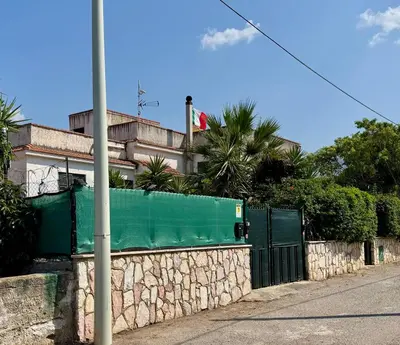 a stone wall with a green fence and a building at Villa Pino in Carini