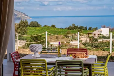 a table with chairs and a plate of food and wine glasses at Villa Orizzonte in Scopello