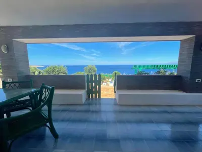 a view of the ocean from a patio with a table and benches at Villa Venere al Sauce - esclusiva villa sul mare in San Vito lo Capo