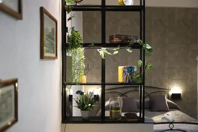 a black shelf with plants on it next to a bed at T&F Casa al Capo - In centro a Palermo in Palermo