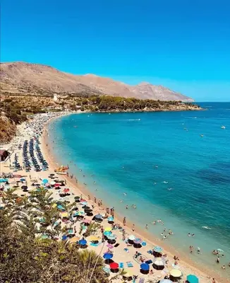 a beach with people and umbrellas and the ocean at Villino Dei Gabbiani in Castellammare del Golfo