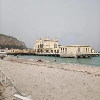 a beach with a pier and buildings in the water at Mondello bed & beach in Palermo