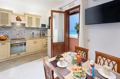 a dining room with a table and a kitchen with the ocean at Beach View Apartment in San Vito lo Capo