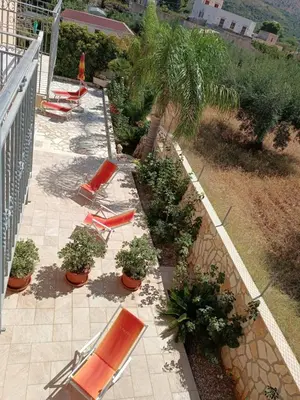 a patio with lounge chairs and palm trees on a balcony at Le Falesie di Castelluzzo in Castelluzzo