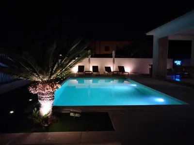 a swimming pool at night with chairs and a palm tree at Villa Marina di Calatubo in Alcamo