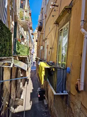 an alley in an old town with a yellow sheet on a balcony at Cattedrale - Maiolica Brugnò in Palermo
