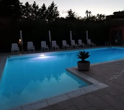 a swimming pool at night with chairs and a potted plant at Borgomare in Campofelice di Roccella