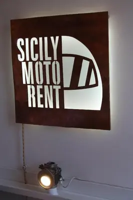 a sign on a wall above a table with a light at Targa Moto Art in Palermo